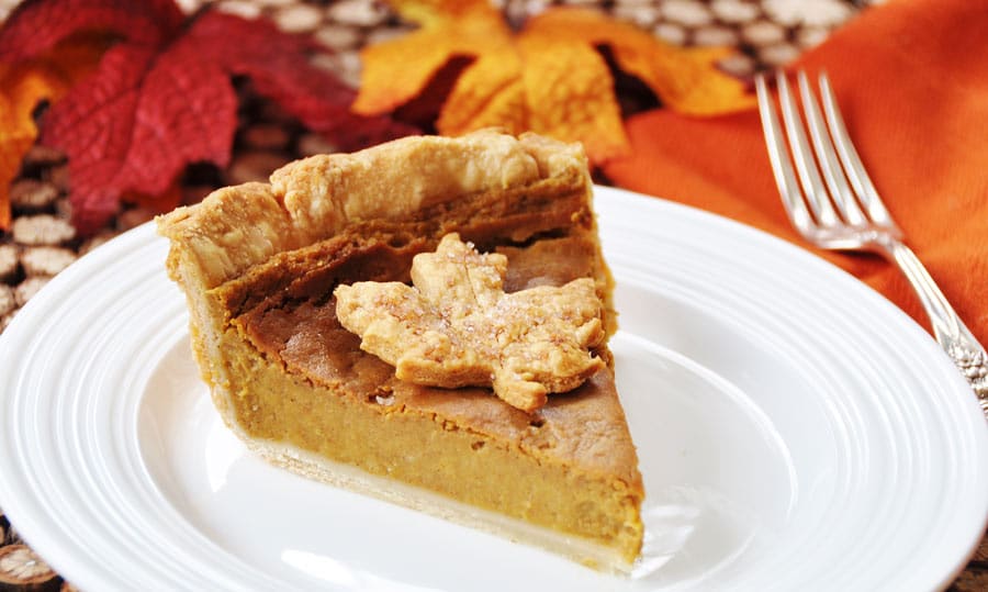 A slice of vegan pumpkin pie with a leaf made out of dough in the center, sitting on a white plate
