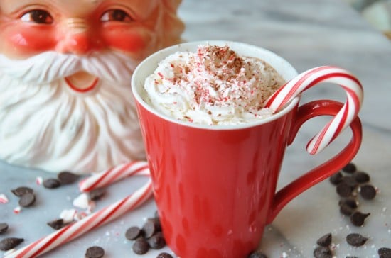 Vegan Peppermint Mocha in a red mug with whipped cream and a candy cane and a Santa cookie jar in the background