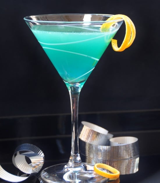 Curacao Martini in a martini glass with a twist of orange rind and silver ribbon on the table