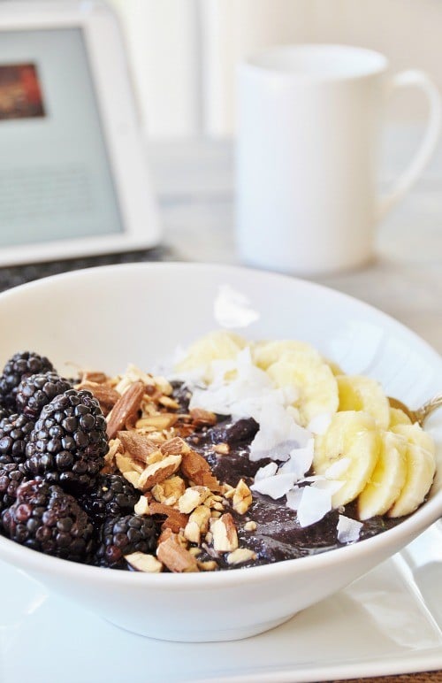 Vegan Berry Banana Smoothie Bowl in a white bowl with a white coffee mug and a laptop in the background