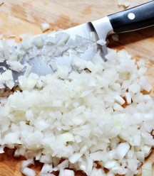 Diced Onions on a wood board with a knife on the board.