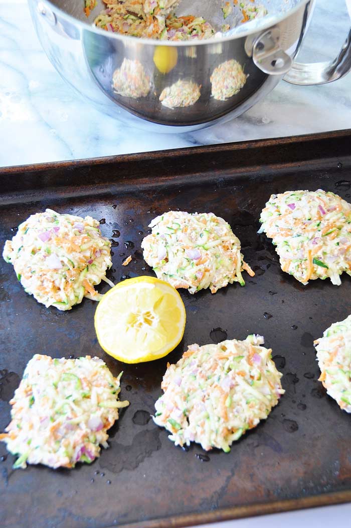 Vegan Oil-Free Zucchini & Carrot Fritters on a baking sheet with a lemon half and the mixing bowl with the batter in the background