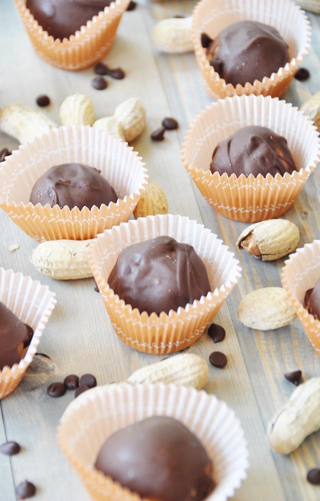 Homemade chocolate candies in muffin cups with chocolate chips and peanuts spread on a wood table.