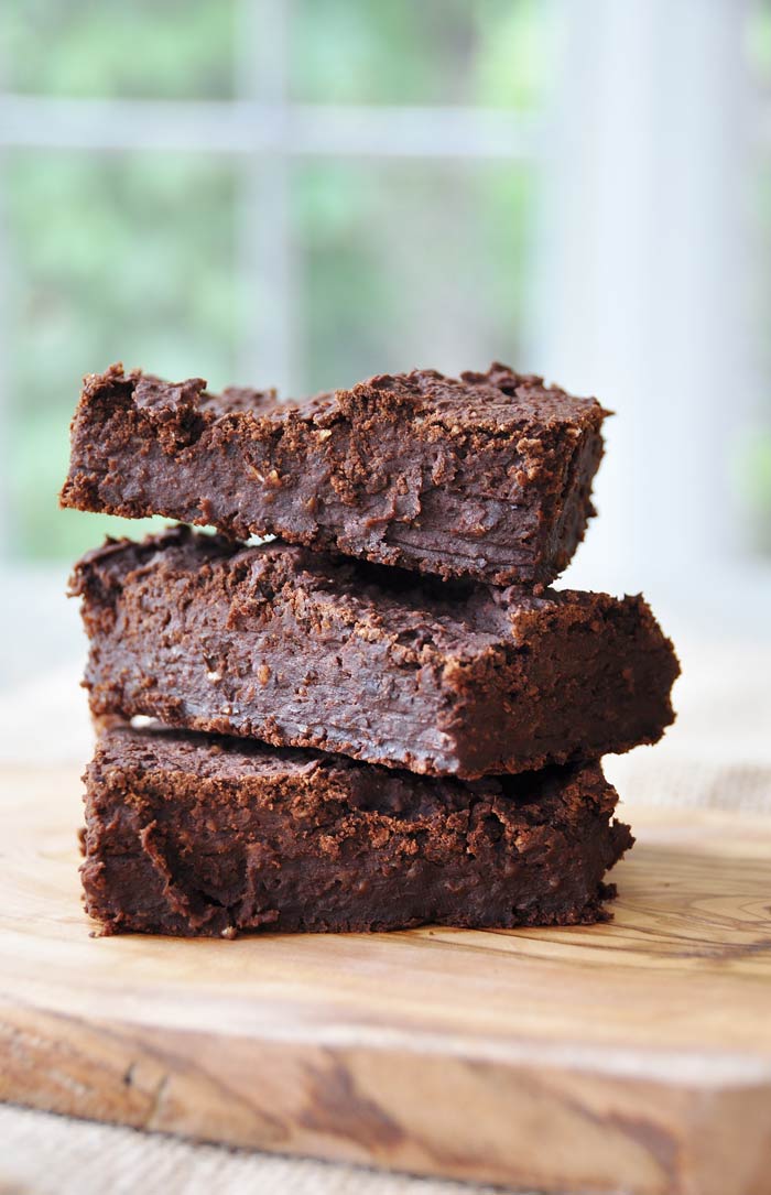 Three brownies stacked on a wood board.