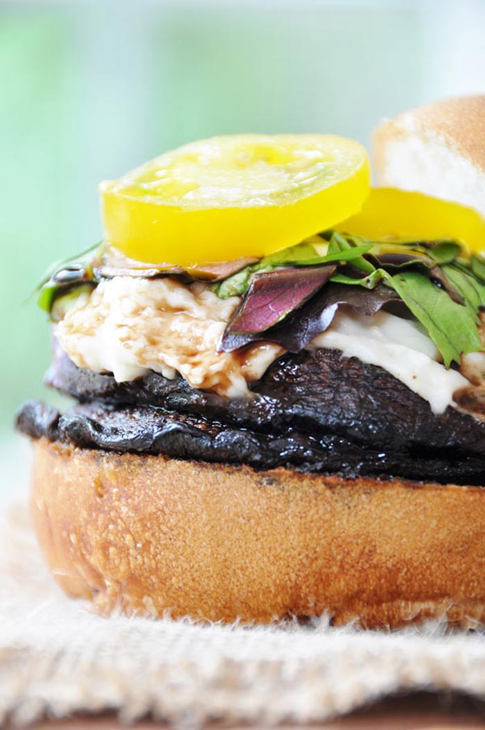 A mushroom burger with mozzarella, lettuce, and a yellow tomato.
