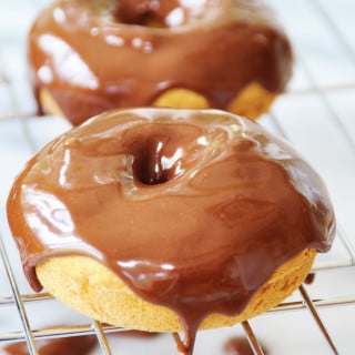 Three pumpkin spice doughnuts with chocolate cinnamon icing covering the tops and dripping down the sides on a wire cooking rack