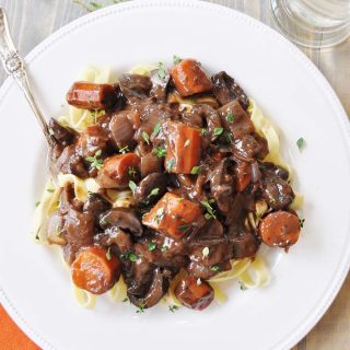 Mushroom Fourguignonne on a white plate with a silver fork and an orange napkin tucked under the bottom left corner of the plate.