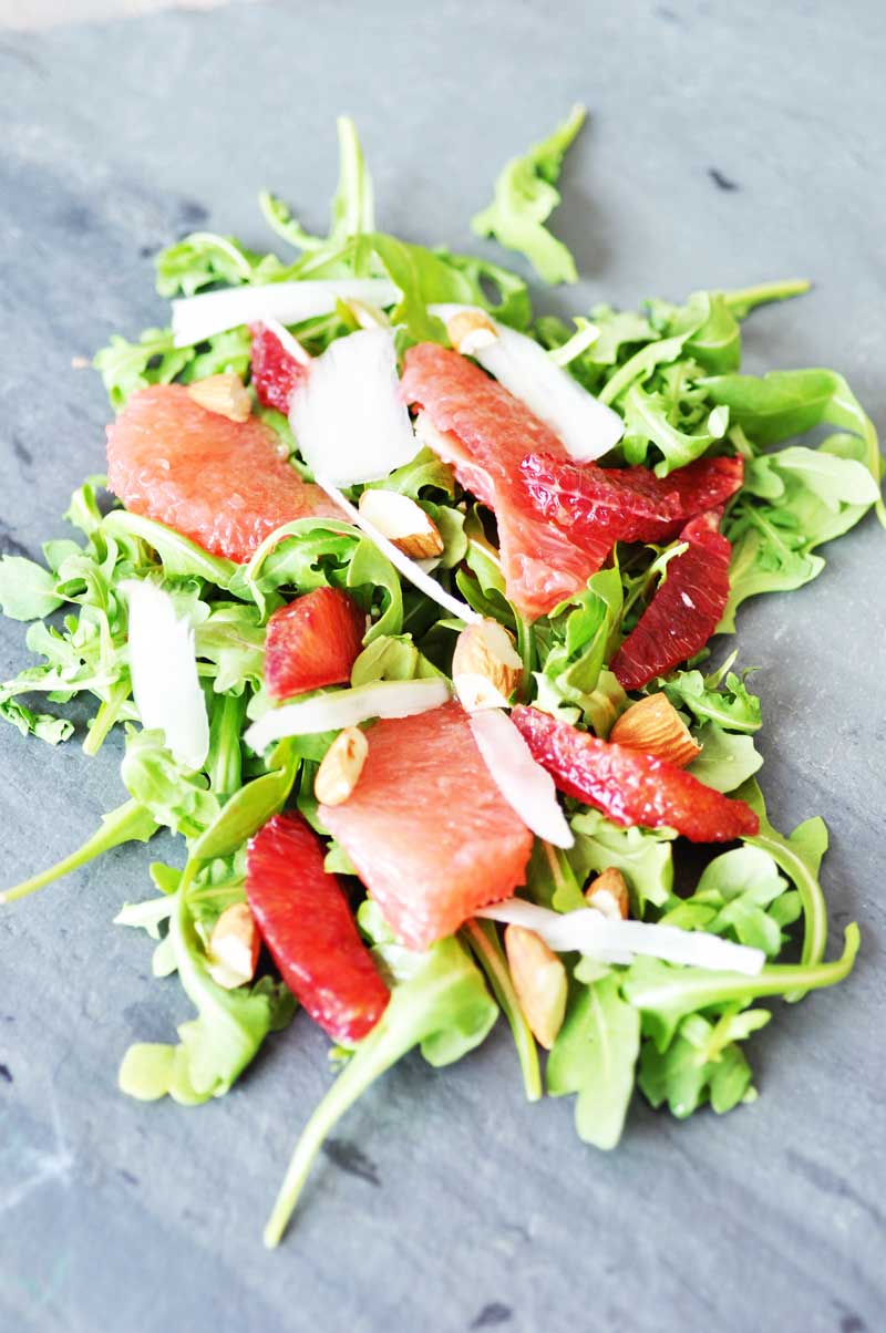 An arugula and citrus salad with chopped nuts on a slate board.