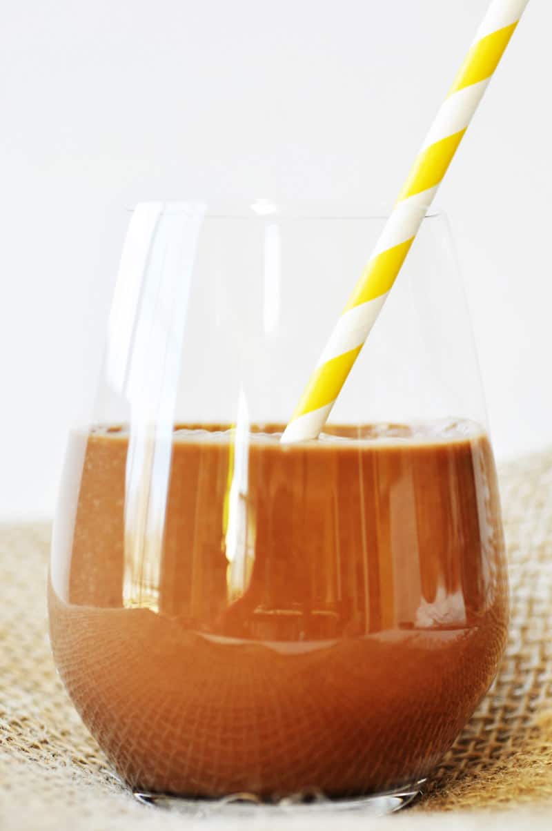 Vegan Chunky Monkey Chocolate Smoothie in a clear glass with a yellow and white striped straw in it.