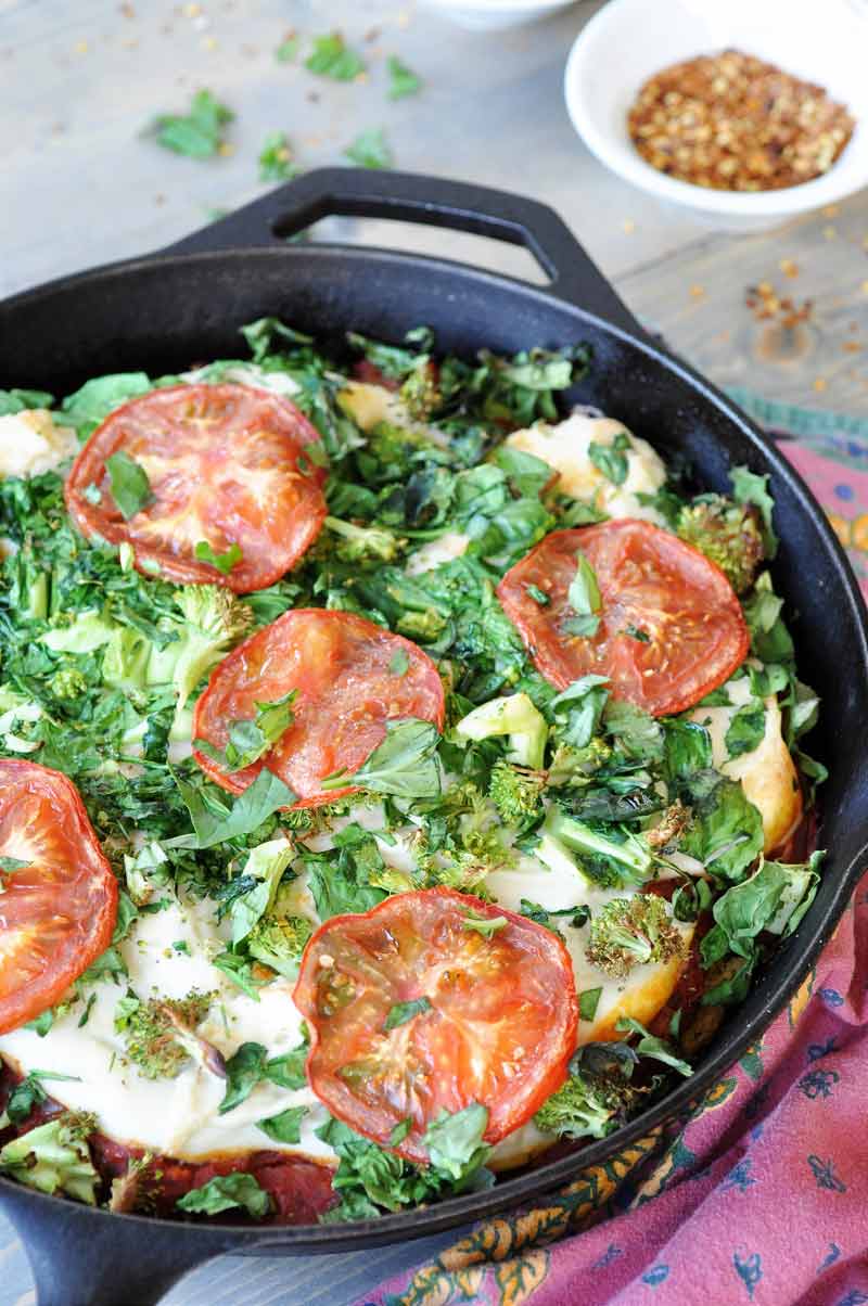 Vegan Deep Dish Pizza in an iron skillet with a red napkin next tothe pan and a white dish of red crushed peppers