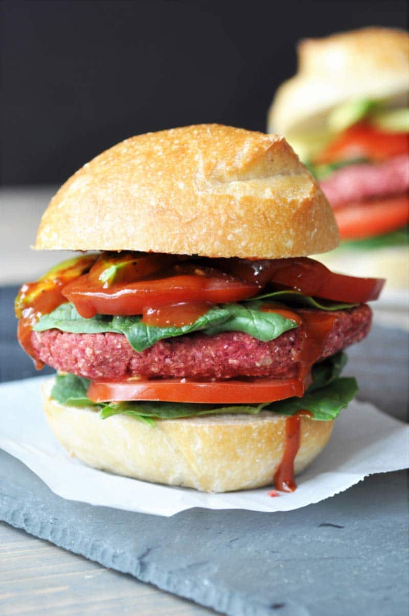 A veggie beet burger with lettuce and tomato and ketchup dripping down the side.