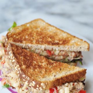 A tuna salad sandwich on toast, cut in half on a white plate.