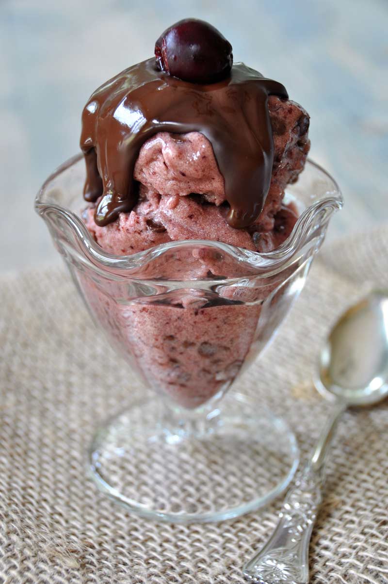 Cherry chocolate chip nice cream in a clear glass ice cream dish with melted chocolate sauce on top and a cherry