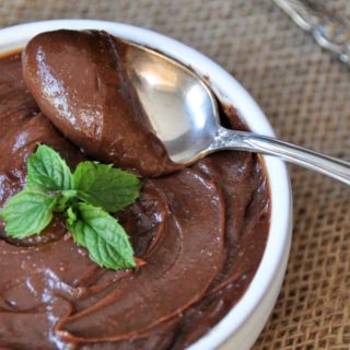 chocolate pudding in a white bowl with a silver spoon taking a scoop of it out of the bowl with a sprig of mint on top