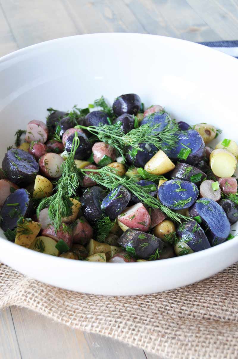 A white bowl filled with tri-colored potato salad on a wood table and a piece of burlap 