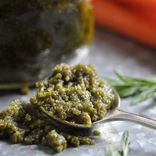 A spoon of pesto on a silver platter with a jar of pesto and carrots in the background