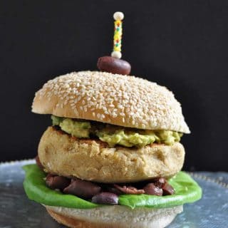 A Hummus burger on a silver plate with an olive stuck on the top with a toothpick