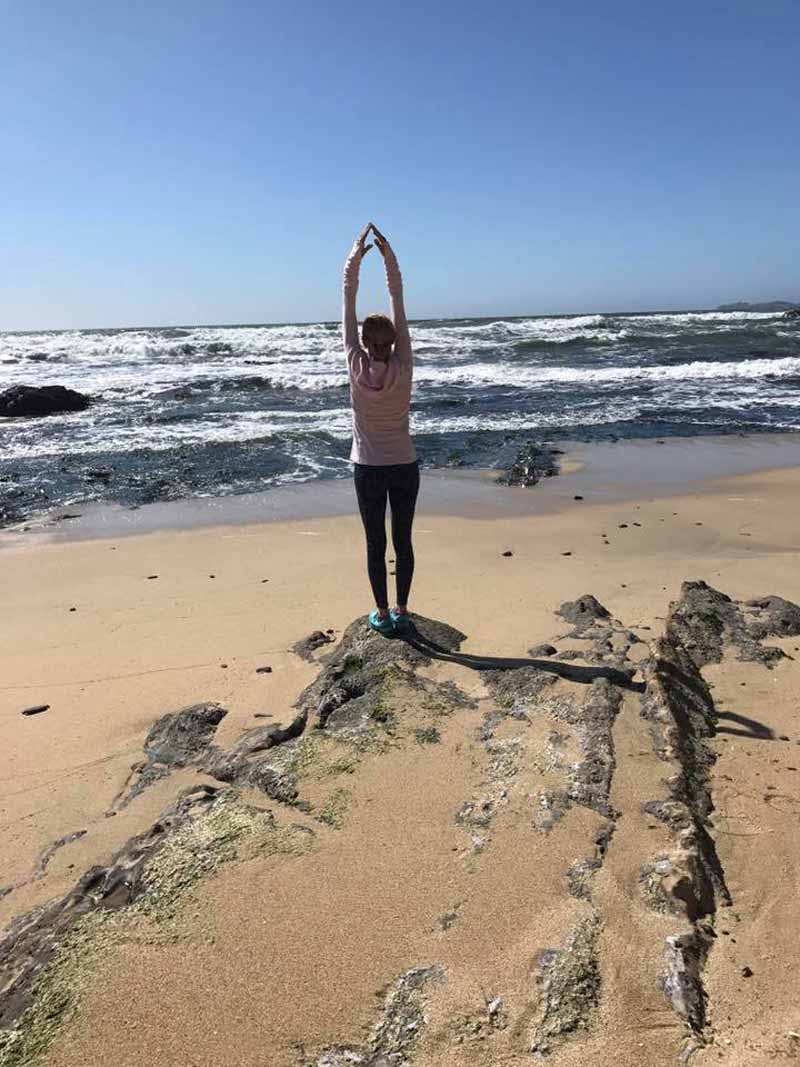 A woman in a pink shirt doing yoga on the beach at Half Moon Bay, CA