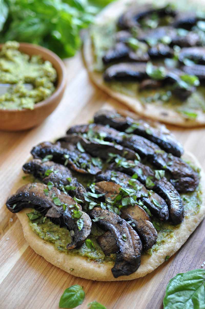 Vegan pesto & Portobello flatbread! on a wooden board with a bowl of pesto and fresh basil leaves on the side