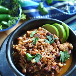 Jamaican jerk chik'n in a black bowl with avocado and cilantro on top and peppers and a striped napkin in the background