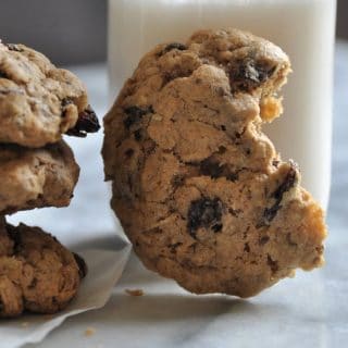 An oatmeal raisin cookie with a bite out of it, leaning on a glass of milk.