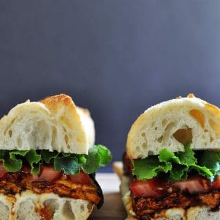 2 halves of an ELT (eggplant, lettuce & tomato) sandwich on a wood board.