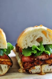 Half of a vegan ELT (eggplant, lettuce & tomato) sandwich with ranch dressing dripping down the side.