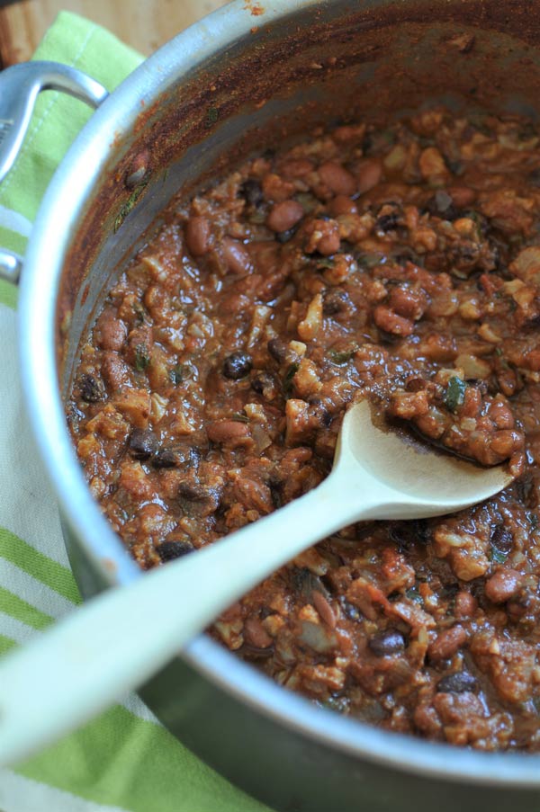 A pot of vegetable chili with a wood spoon in it and a green and white striped towel next to it.