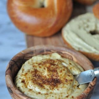 Vegan pumpkin spread in a wooden bowl with bagels on a wood board.