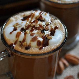Homemade Vegan Maple Pecan Lattes in clear mugs with foamy milk and a drizzle of maple syrup and crushed pecans on top