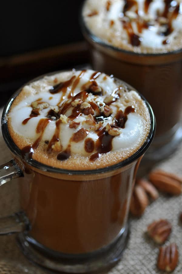 Homemade Vegan Maple Pecan Lattes in clear mugs with foamy milk and a drizzle of maple syrup and crushed pecans on top