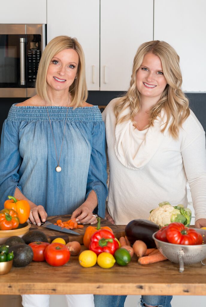 A picture of Linda and Alex standing next to a wooden table with lots of colorful vegetables.