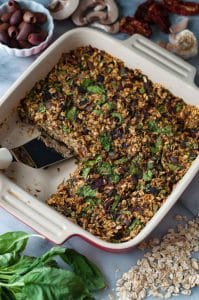 A red and white ceramic pan with baked savory oats, one piece is missing and there's a spatula in the pan