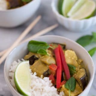 A bowl of green vegetable curry with rice and a slice of lime in a white bowl with chopsticks on the marble table