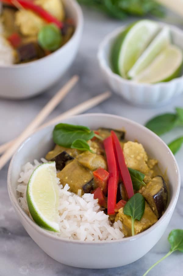 A bowl of green vegetable curry with rice and a slice of lime in a white bowl with chopsticks on the marble table