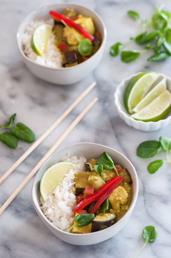 Green Vegetable Curry i na white bowl sitting on gray marble with chopsticks and a bowl of limes