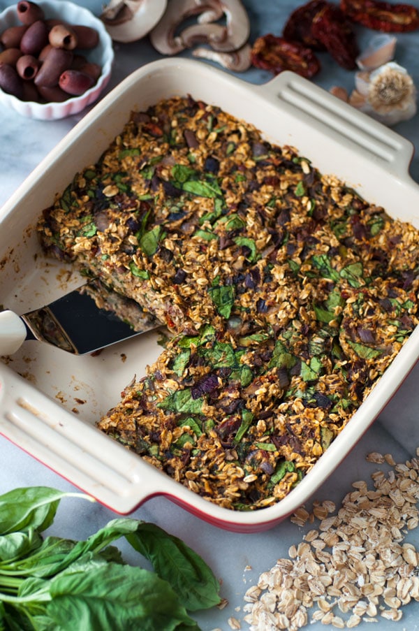 A pan of savory vegan baked oatmeal with a piece missing and a spatula in the pan
