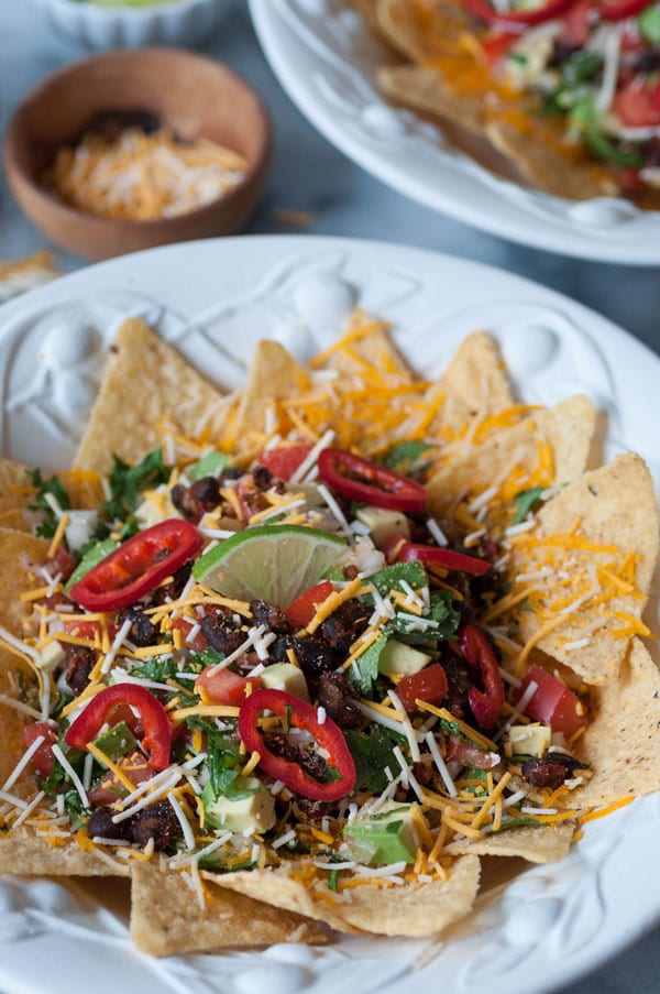 Two white bowls filled with vegan nacho bowls and a wooden bowl of vegan cheese shreds in the background