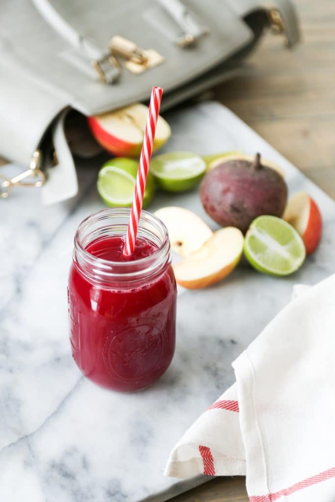 Mason Jar filled with juice with a beet, apples, and limes in the background