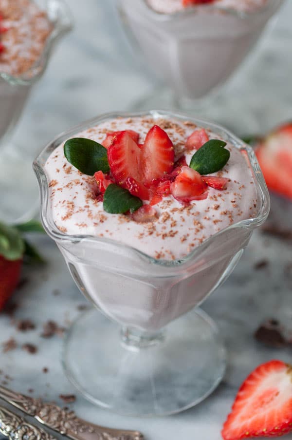 3 dishes of raw vegan strawberry mousse in glass dishes, garnished with chopped strawberries and shaved dark chocolate.
