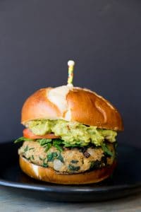 A spinach burger on a bun with avocado and tomato with a toothpick stuck in the center.