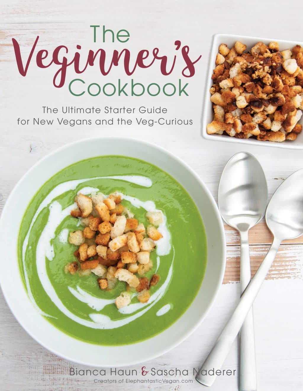 The cover of the Veginner's Cookbook with a white background a bowl of green soup in a white bowl with croutons on top, two silver spoons criss-crossed and a bowl of croutons in the corner
