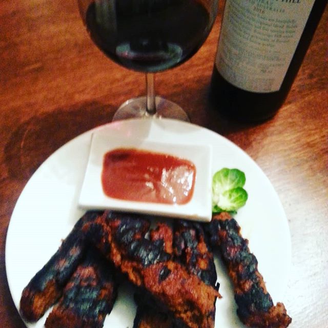 A white plate with vegan BBQ Ribz and a glass of red wine and the bottle next to it. 