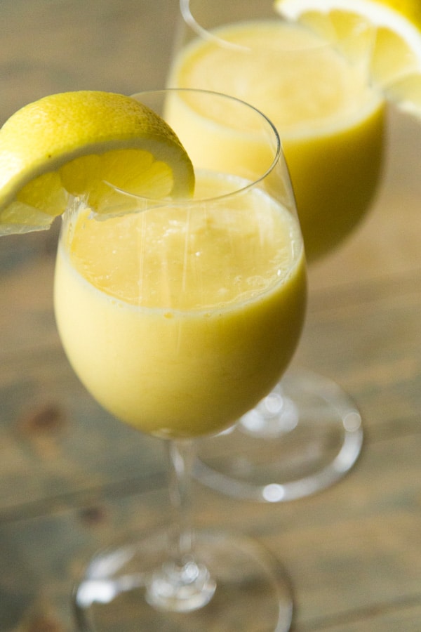 two stemmed wine glasses filled with lemon slushies with lemon wedges on the rim