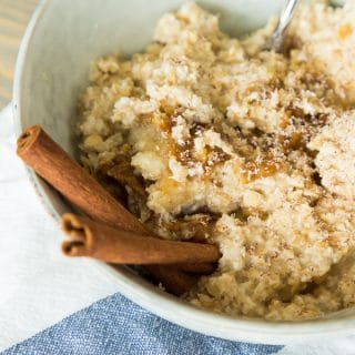 apple cinnamon overnight oats with cinnamon sticks, blue bowl, and napkin on wood board
