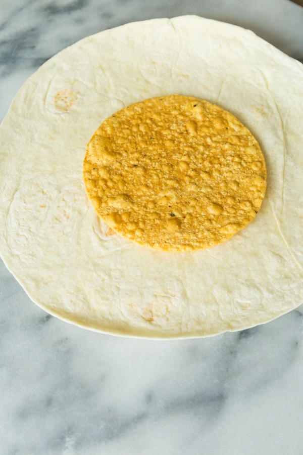 A large flour tortilla with a corn tostada shell in the center on a marble surface