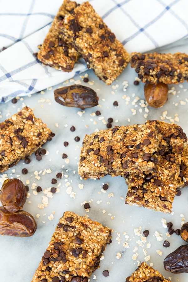 Vanilla Chip Buckwheat Bars scattered on a marble surface with chocolate chips, oats, and dates