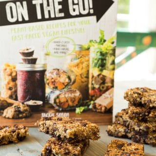 Vegan Yack Attack On the Go Cookbook standing on a table with Vanilla Chip Buckwheat Bars scattered on the table in front of it.