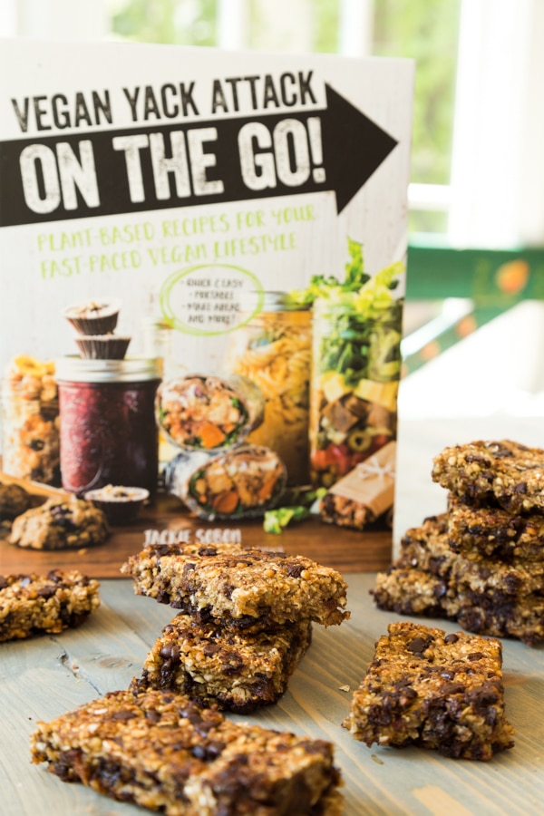 Vegan Yack Attack On the Go Cookbook standing on a table with Vanilla Chip Buckwheat Bars scattered on the table in front of it.