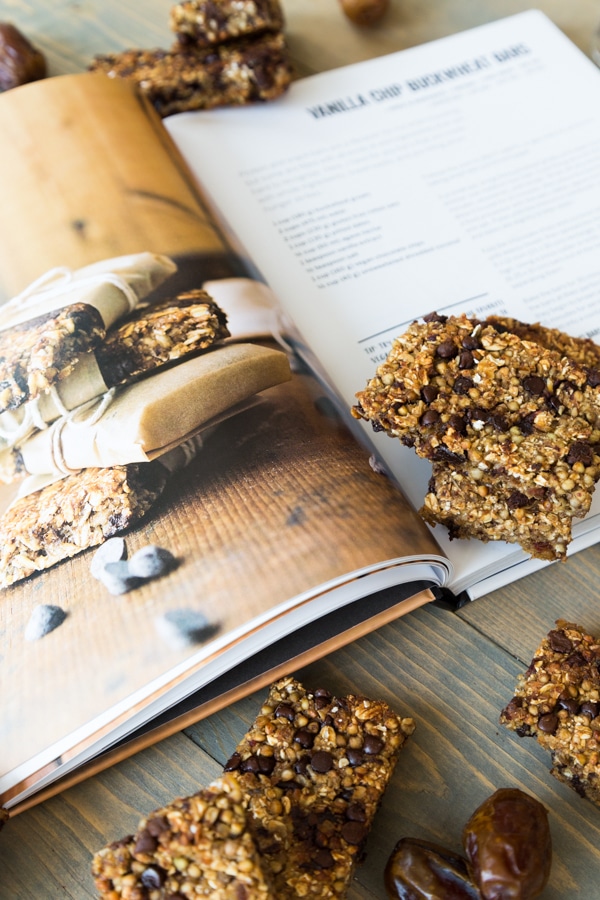 An open page of vanilla chip buckwheat bars in the Vegan Yack Attack On the Go cookbook and the cooked bars scattered next to the book